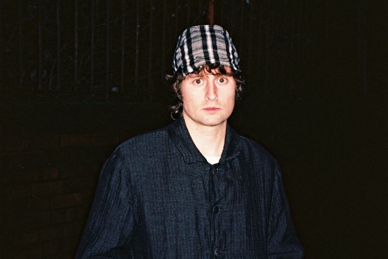 Australian DJ and producer Mall Grab wearing a plaid cap and dark jacket posing at night in a promo portrait.